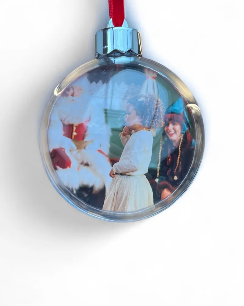 A red bauble on a ribbon with a family’s photo with Santa inside it